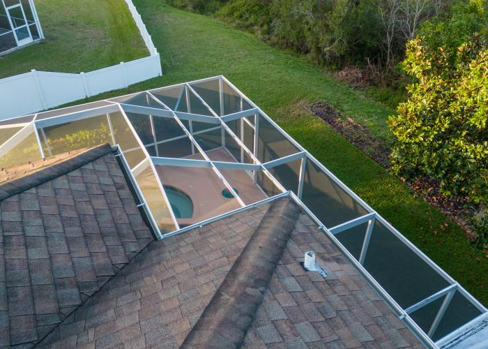 Drone picture of a pool enclosed by a screen enclosure with roof and patio in Florida during sunset